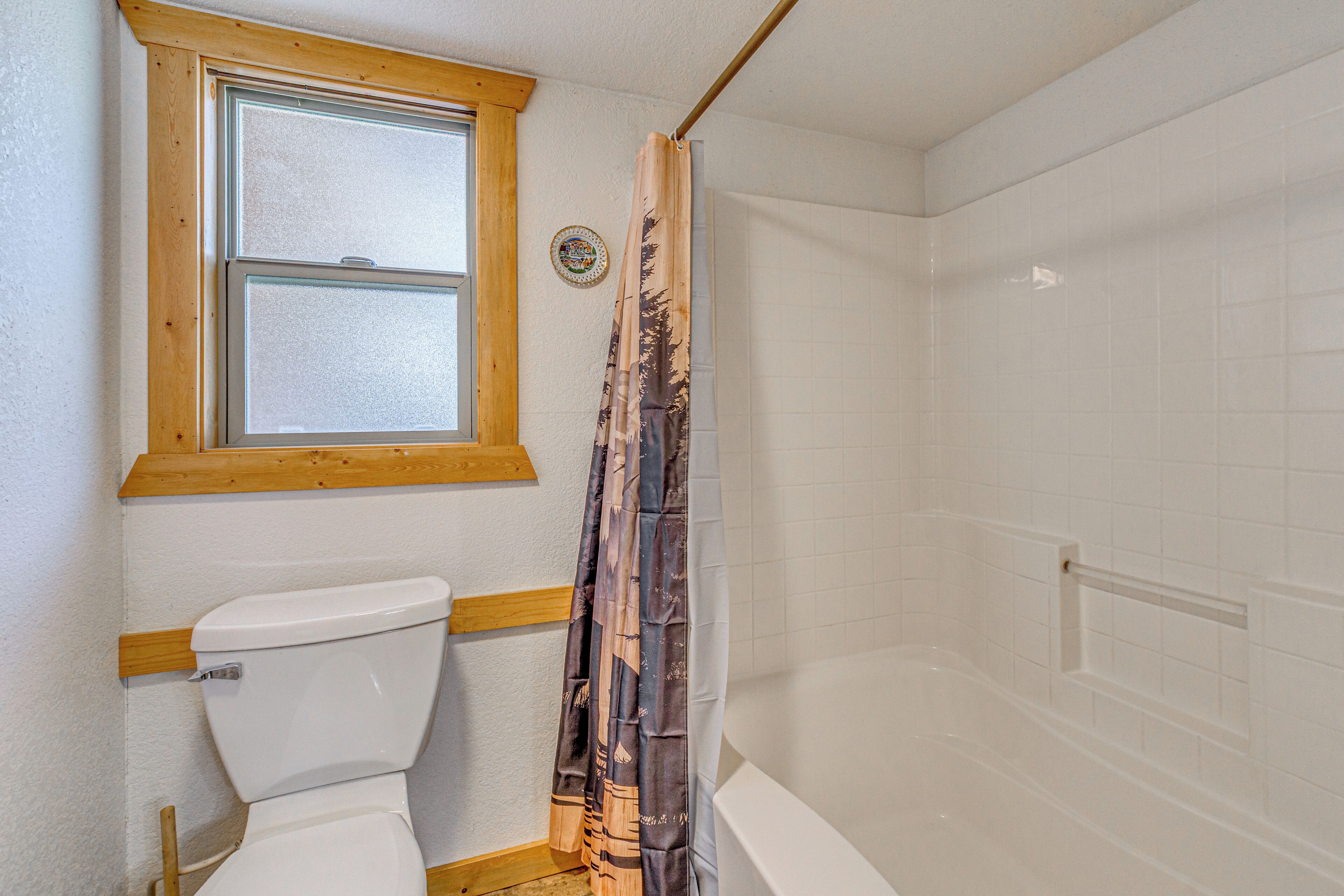 A bathroom with a toilet, a shower curtain, a window, and a bathtub.