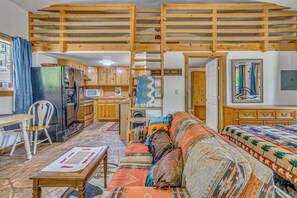 Ein gemütliches Zimmer mit Holzbalkendecke, einer Couch, einem Tisch, einem Bett und einer Küchenzeile.