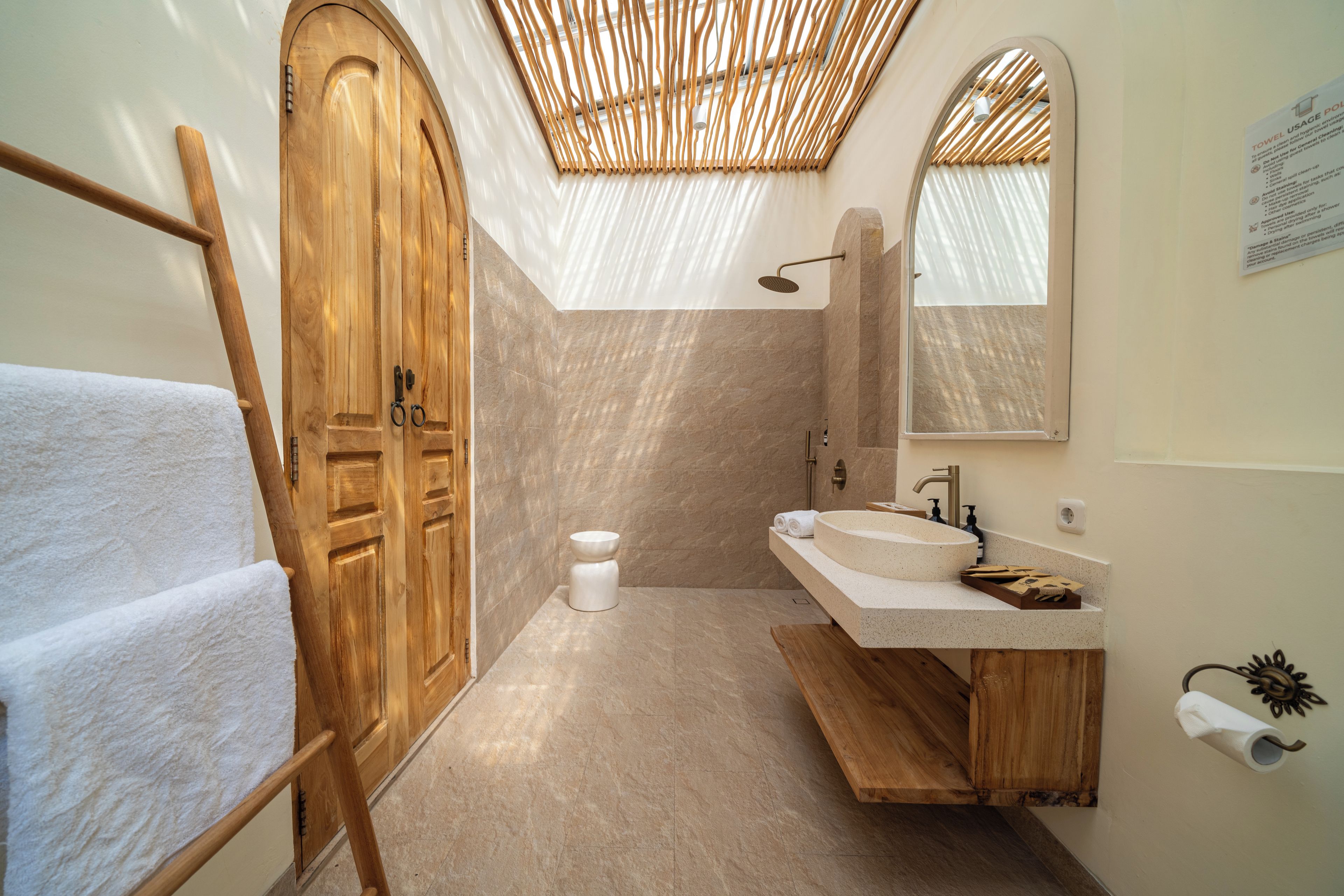 A bathroom with a wooden door, a shower, a sink, and a towel rack.