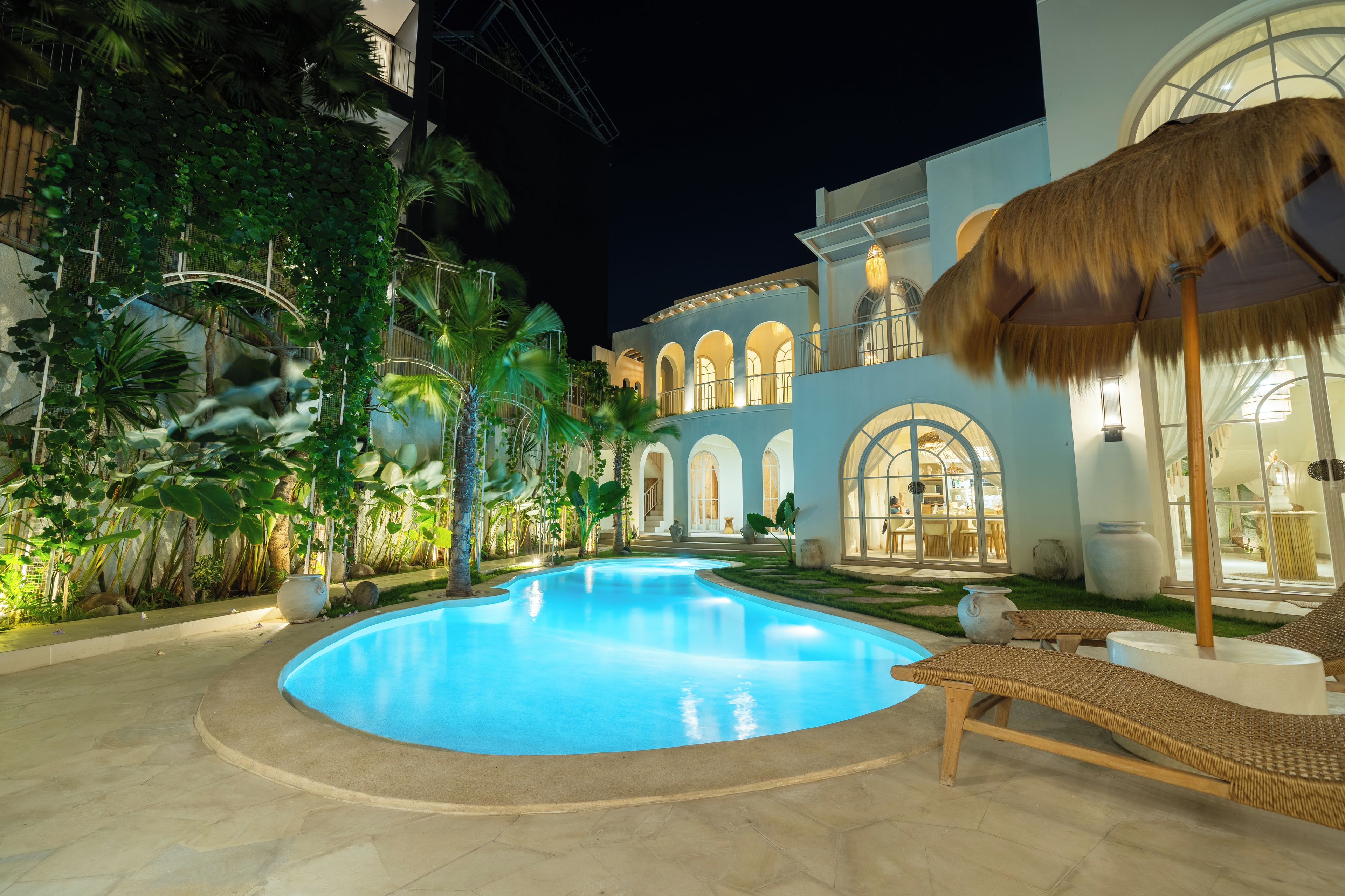 A swimming pool surrounded by lush greenery and a building with arched windows.