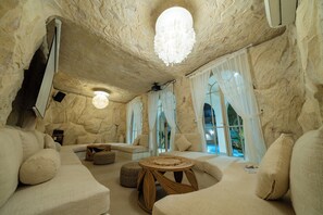 A cozy interior with stone walls, a round table, and comfortable seating. - Velin Villa (Canggu)