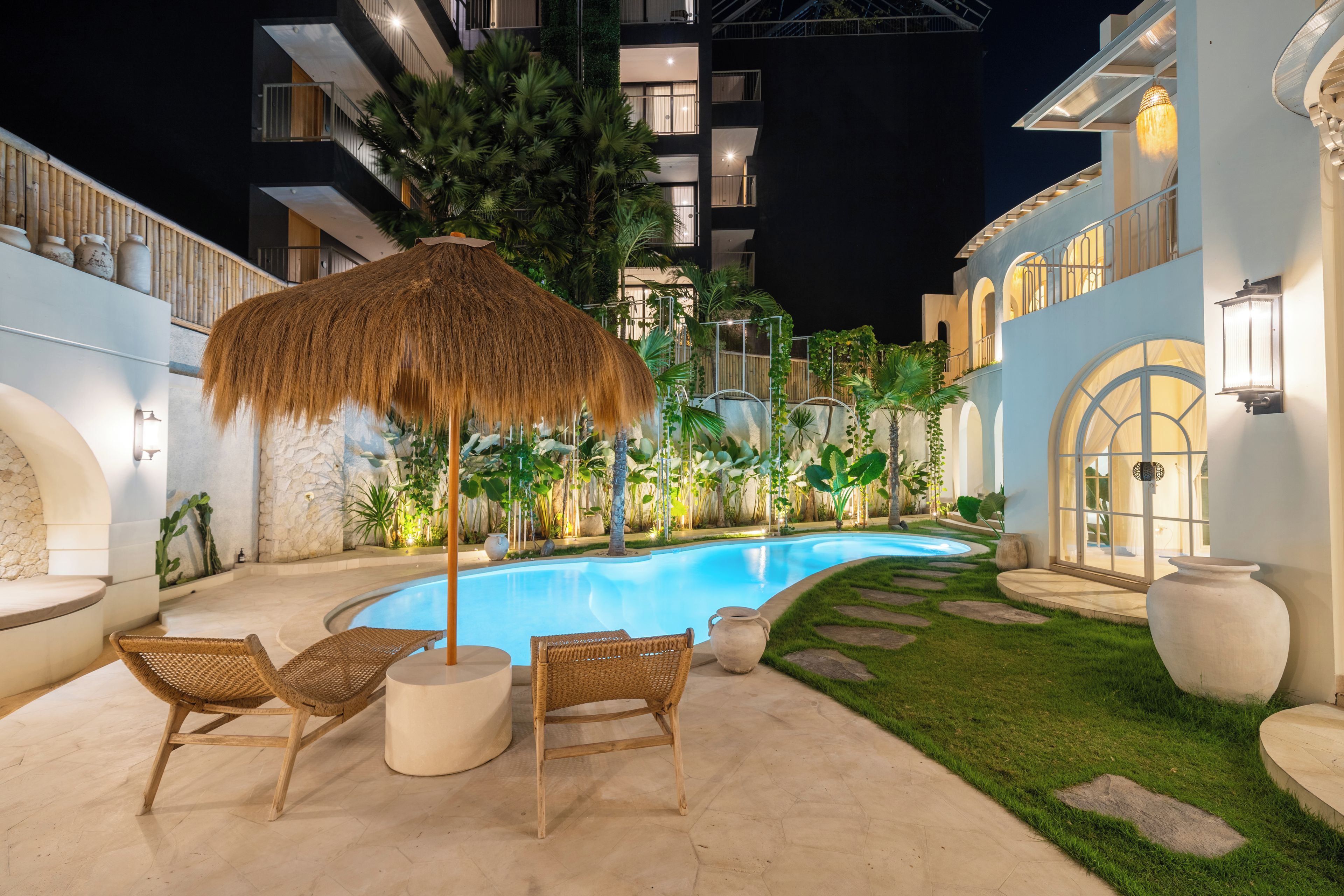 A swimming pool area with lounge chairs and a thatched umbrella.