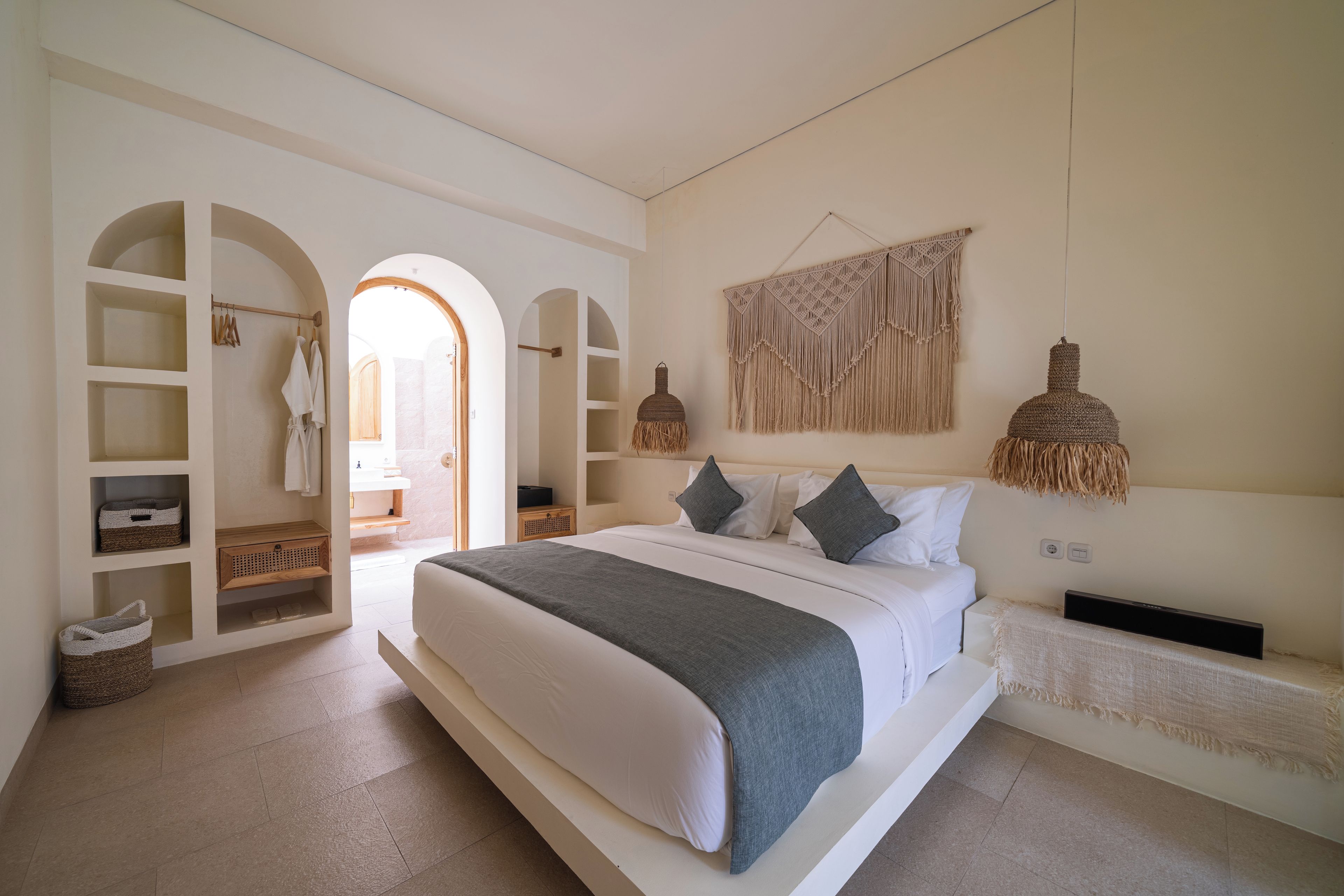 Un dormitorio con una cama grande, estanterías empotradas, un tapiz de macramé y una lámpara tejida.