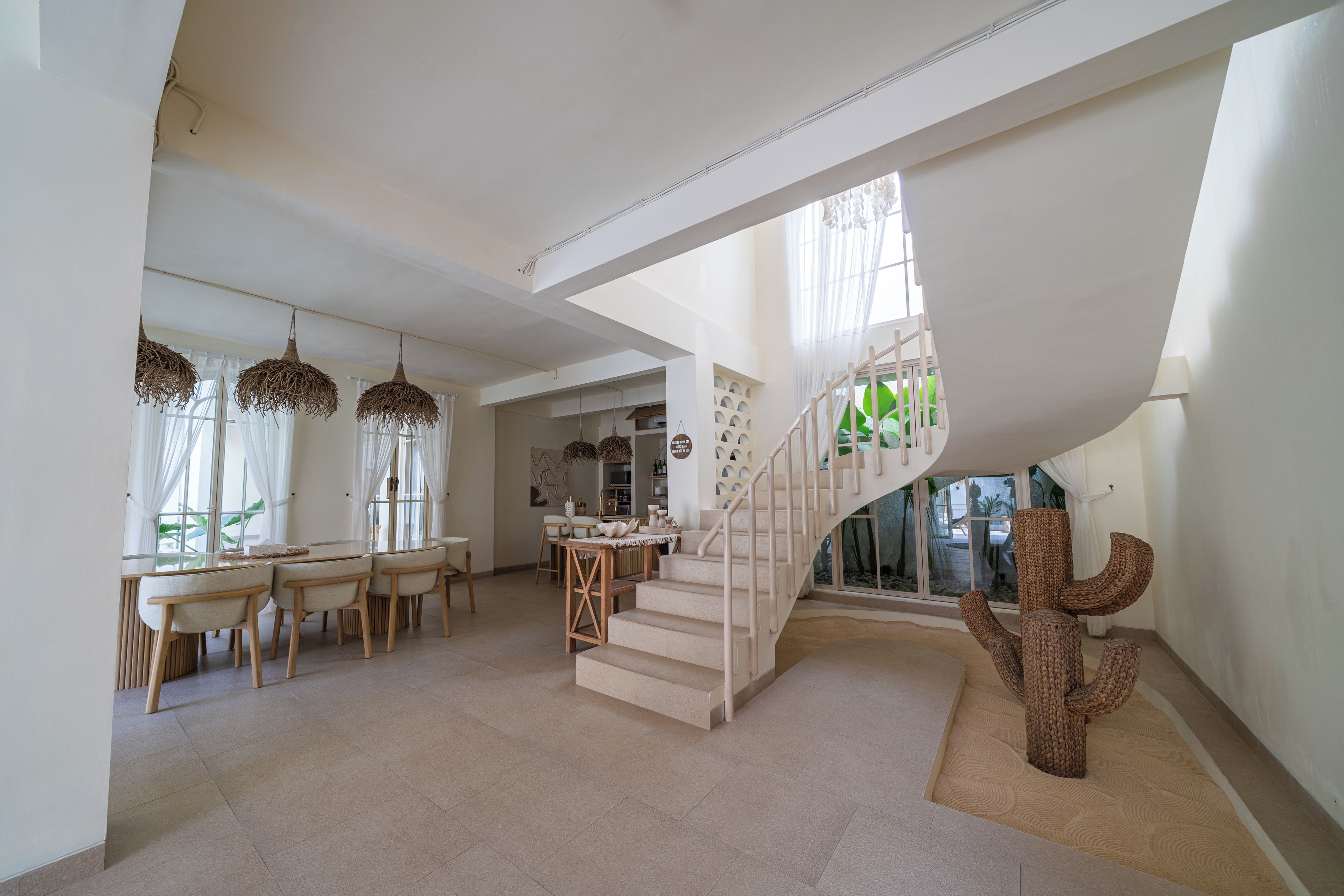 Un interior espacioso con una escalera moderna, un comedor y una escultura de cactus.