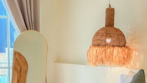 En säng med en vit sänggavel, en hängande, vävd lampa, en grön kudde och en stol med ett ryggstöd i trä.