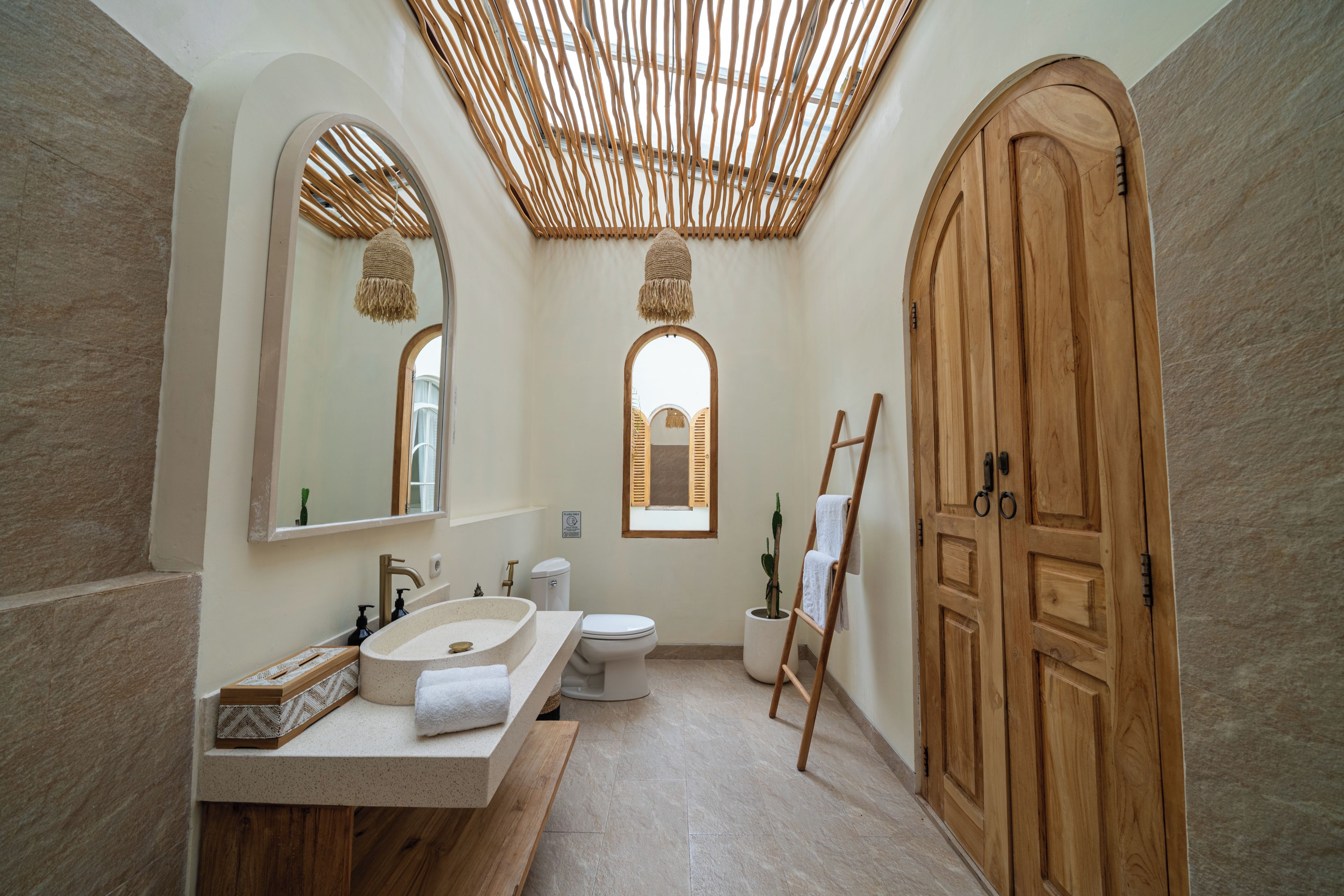 Un baño con tocador de madera, inodoro y puerta grande de madera.