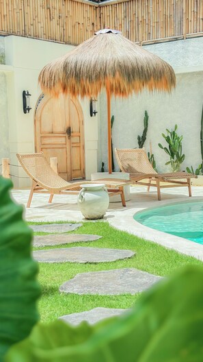 A poolside area with lounge chairs, a thatched umbrella, a wooden door, and cacti. - Velin Villa (Canggu)
