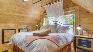 A wooden cabin bedroom with a bed, bedside tables, a nightstand, a window with a view, and a ceiling fan. - Hike, Bike, Tubing, Whitewater Rafting! Saluda Gem (Saluda)