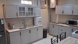 Una cocina con armarios, un lavamanos, un microondas y un cubo de basura.