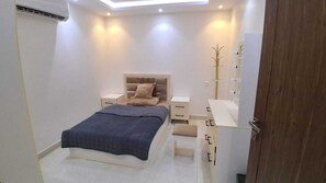 Un dormitorio con cama, mesitas de noche, un armario y un perchero.