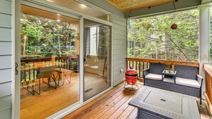 Eine überdachte Terrasse mit Schiebetür, Grill, Gartenmöbeln und Blick auf einen Garten.