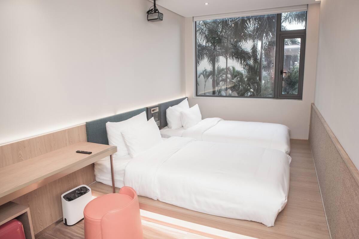 Una habitación de hotel moderna con un gran ventanal, una cama, un escritorio y un cesto de basura.