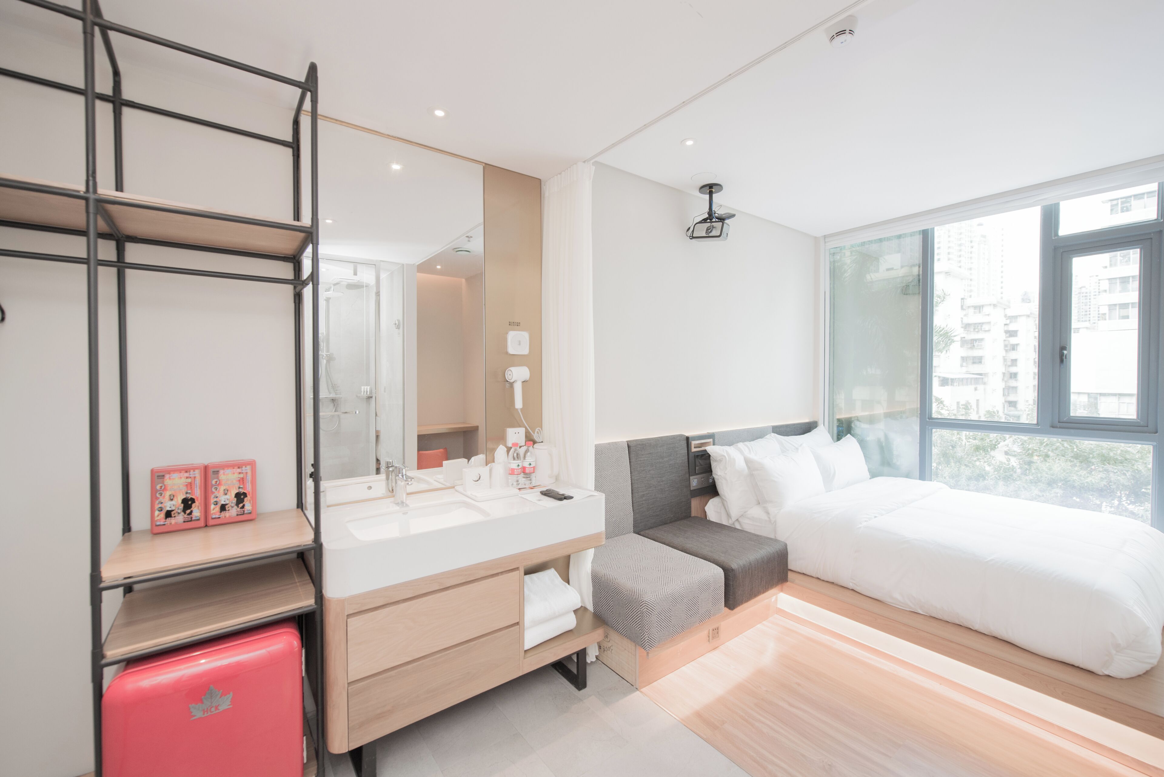 A modern hotel room with a large bed, a vanity with a mirror, a small seating area, and a window with a city view.
