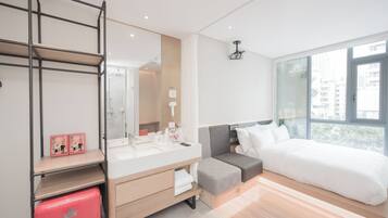 A modern hotel room with a large bed, a vanity with a mirror, a small seating area, and a window with a city view.