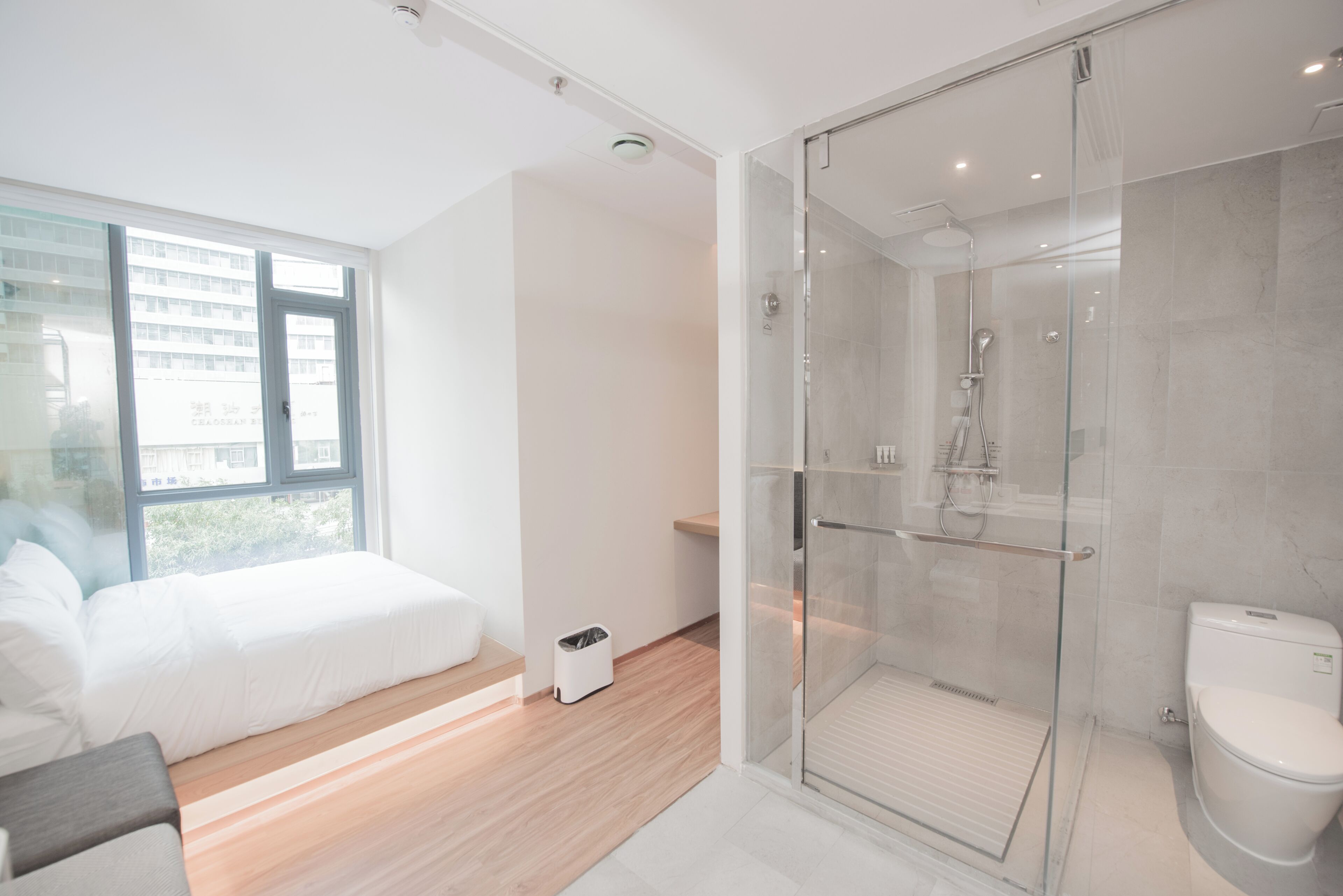 Une salle de bain moderne avec une douche en verre, des toilettes et un lit donnant sur un bâtiment à l’extérieur.