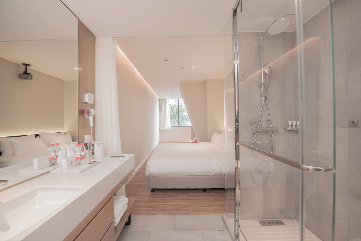 Una habitación de hotel moderna con un espejo grande, un baño independiente, una cama y zona de ducha.