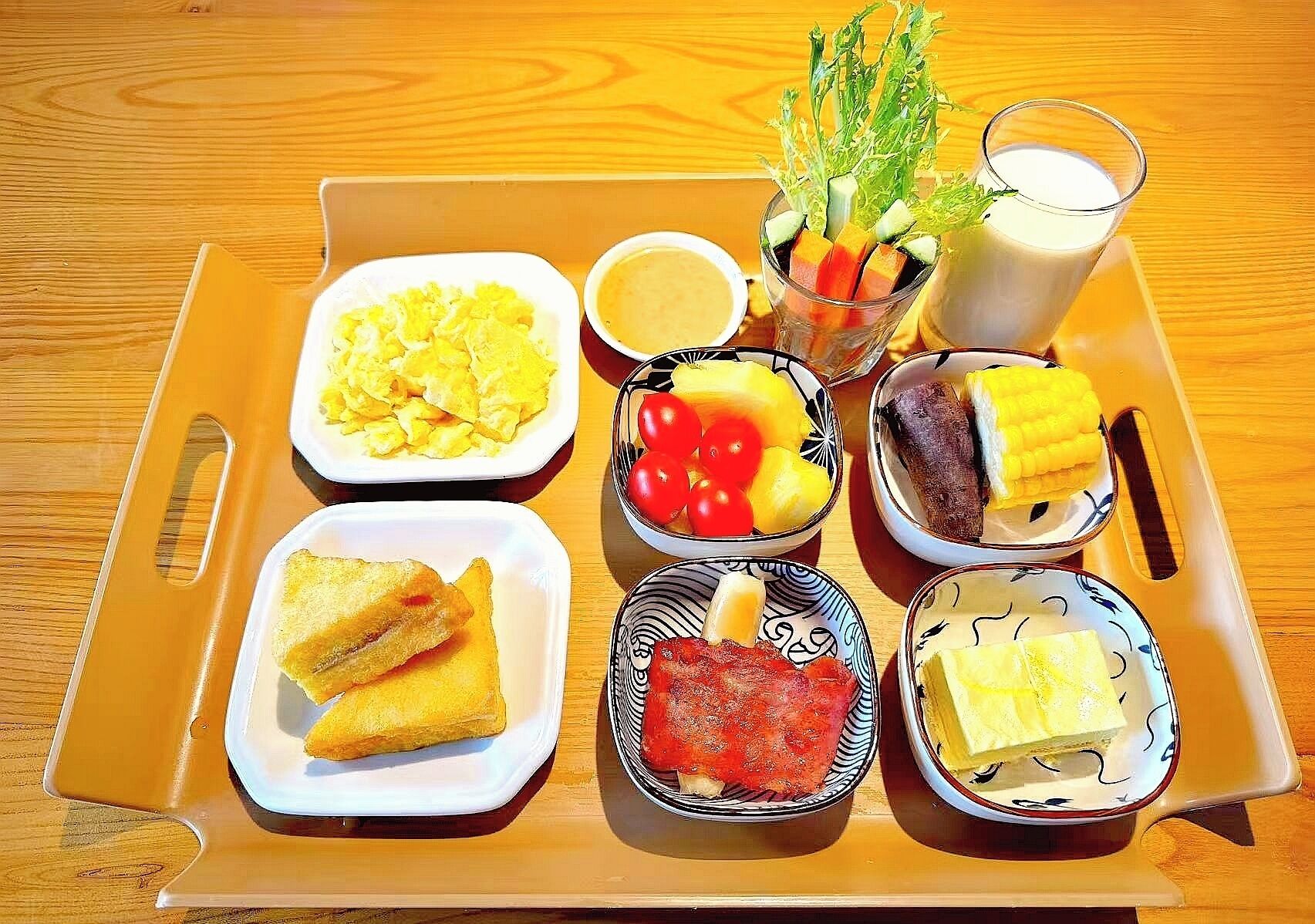 A tray with various breakfast items including scrambled eggs, toast, fruit, and a glass of milk.