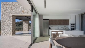 Een moderne keuken met een stenen gevel, een eetgedeelte met een ronde tafel, en uitzicht op de omgeving.