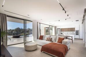 A modern living room with a sofa, ottoman, and a view of the outdoors. - Aeora Villa, Shoreline Getaway (Chania)