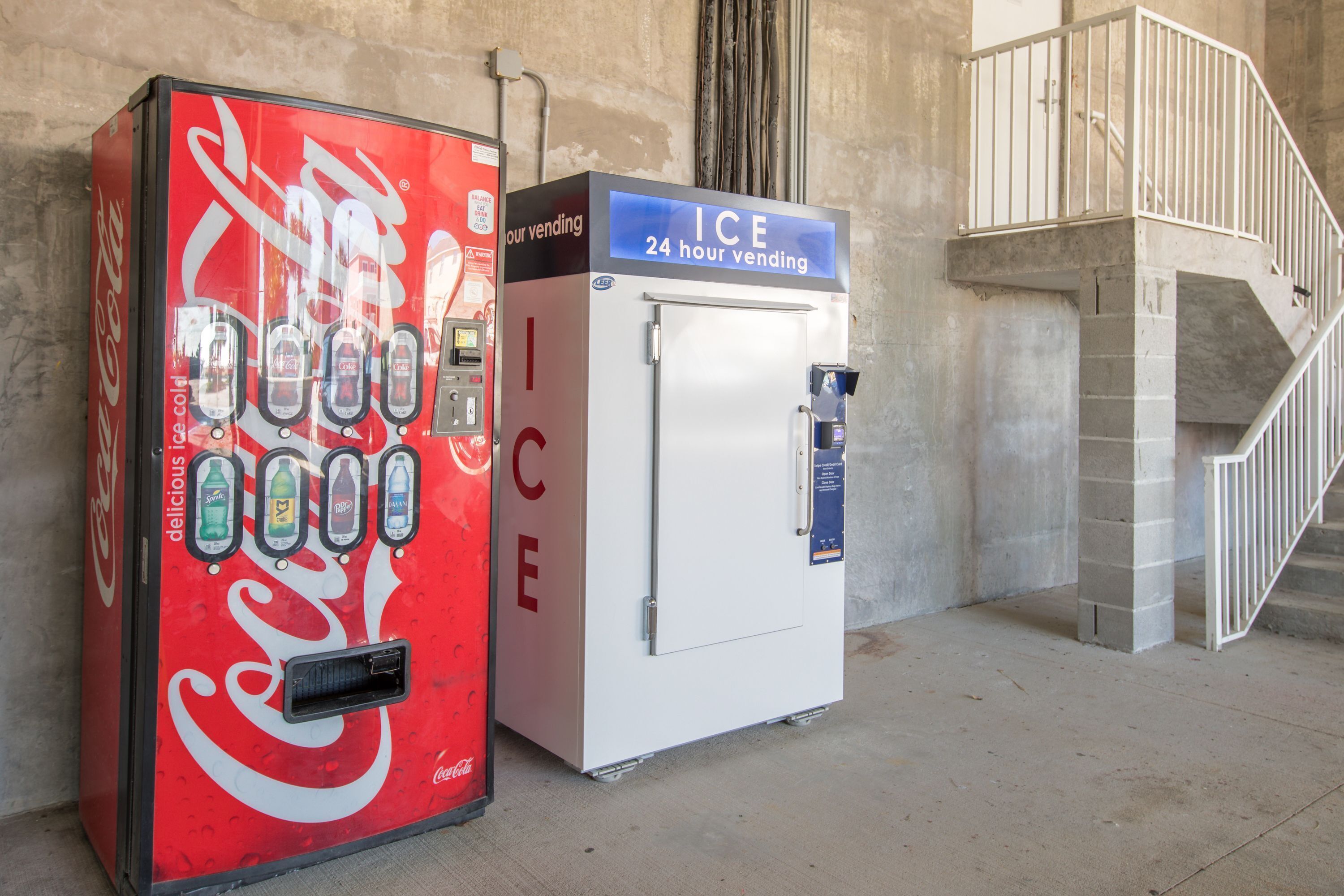 Een Coca-Cola automaat en een ICE 24-uurs automaat naast een trap.