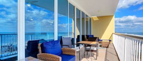 A balcony with wicker furniture, a table, and a view of the ocean.