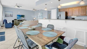A spacious dining area with a wooden table, multiple chairs, ceiling fans, and pendant lighting. - Sanibel 1005 by Hosteeva (Gulf Shores)