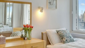 A bedroom with a bed, a bedside table, a mirror, a window, and a view of the city. - LuxeLet St Giles Duplex Penthouse  (London)