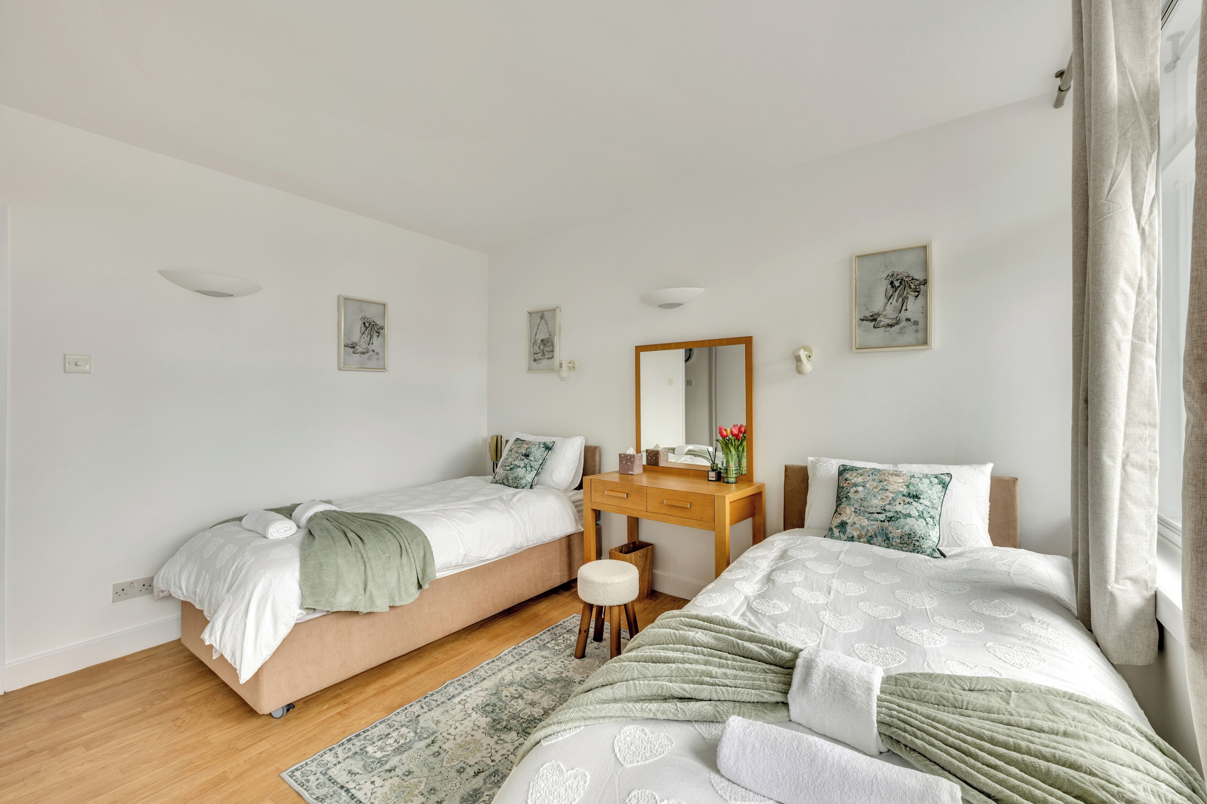 A bedroom with two beds, a wooden dresser, a mirror, and a small stool.