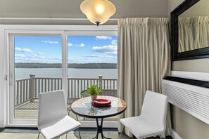 Uma varanda com vista para um lago, uma mesa redonda com um vaso de planta e duas cadeiras.