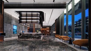 A modern lobby with a marble floor, a reception desk, and seating area with orange chairs. - IntercityHotel Shanghai Pujiang Center (Shanghai)