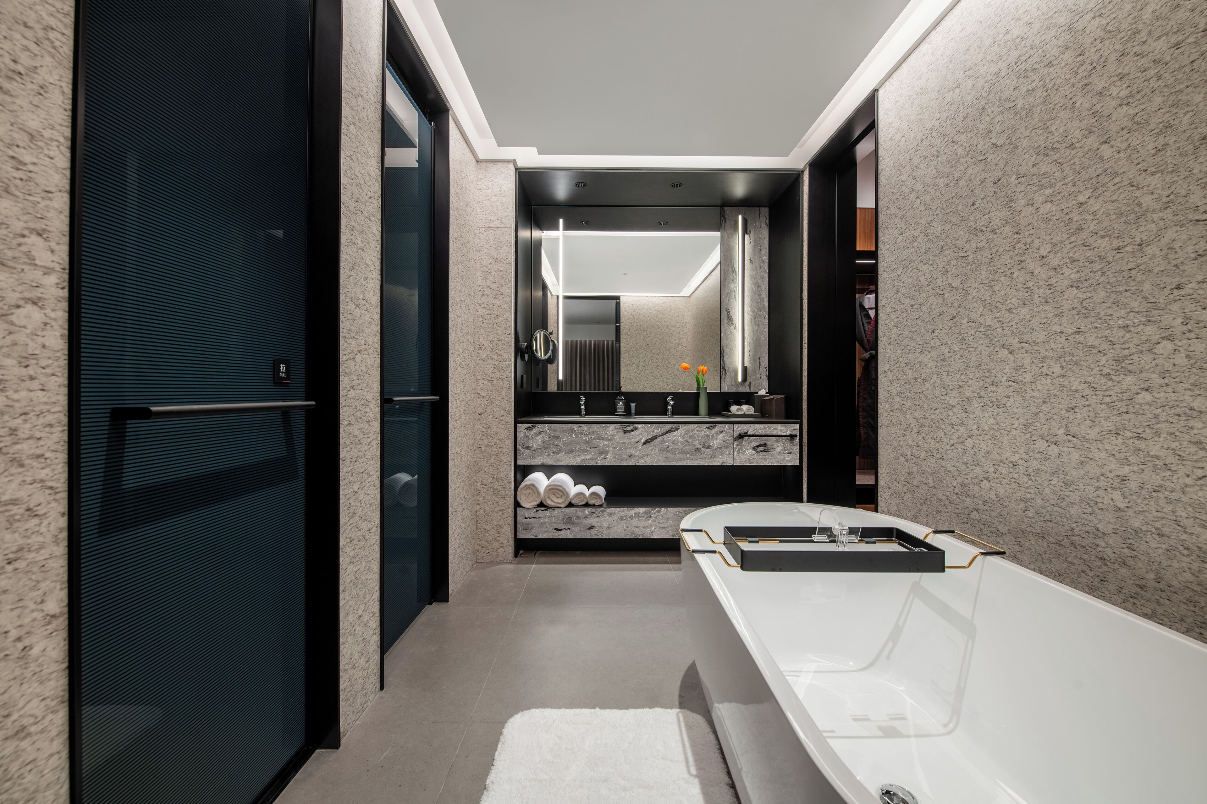 A modern bathroom with a large mirror, a bathtub, and a vanity with a marble countertop.