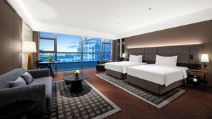 Ett modernt hotellrum med ett stort fönster, två sängar, en soffa, ett litet bord och ett nattduksbord.
