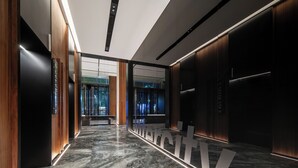 En modern entréhall för hissar med marmorgolv, trädetaljer och en stor, upplyst skylt.