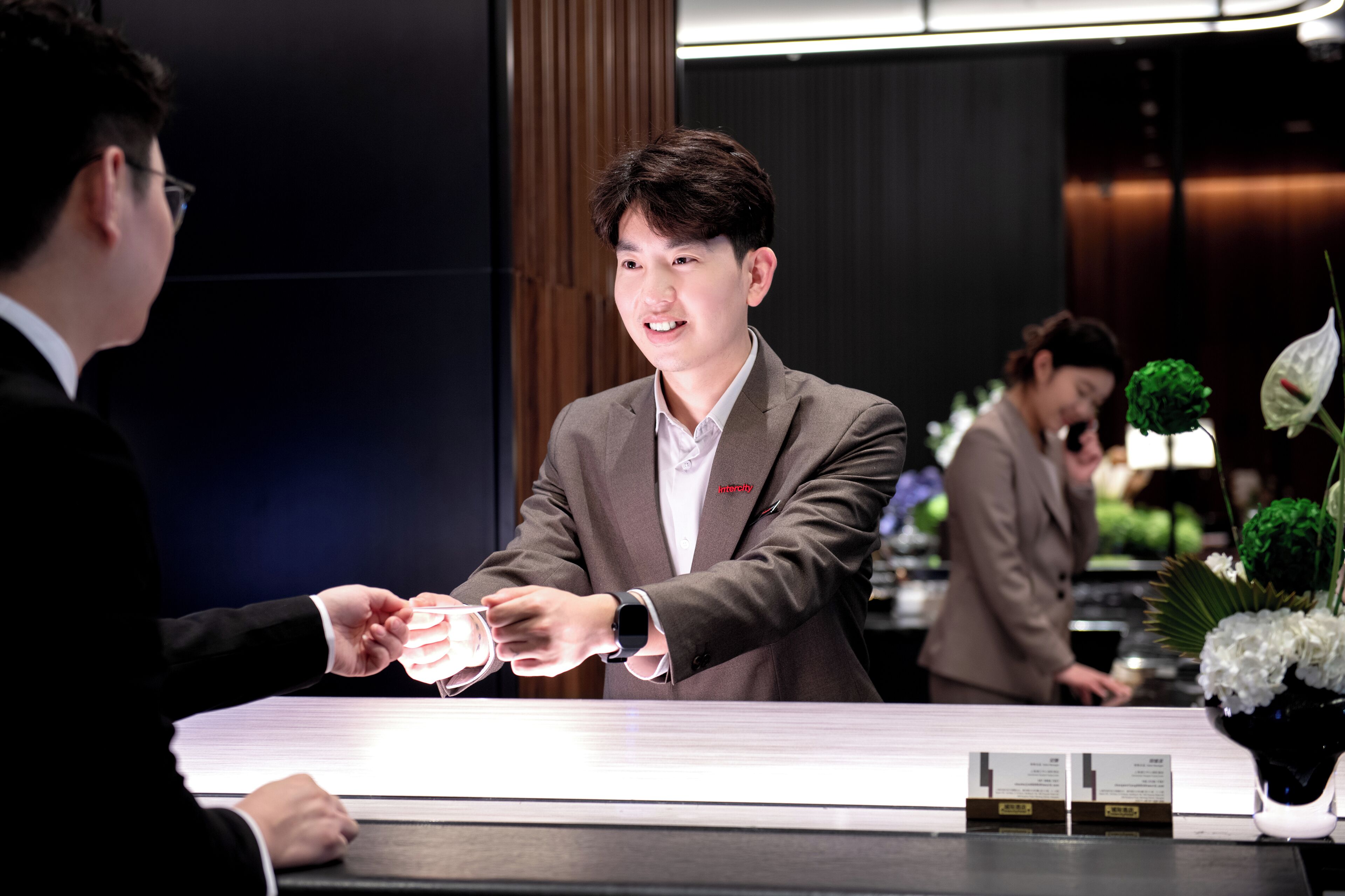 A man in a suit handing over a card to another man at a reception desk.