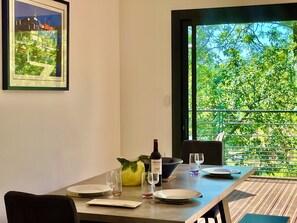 Une table à manger dressée avec des assiettes, des verres, une bouteille et un saladier, donnant sur un paysage verdoyant.