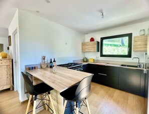 A modern kitchen with a wooden table, black chairs, a stove, and a window overlooking greenery. - Le Refuge de Souspierre - Calm & disconnection (Souspierre)