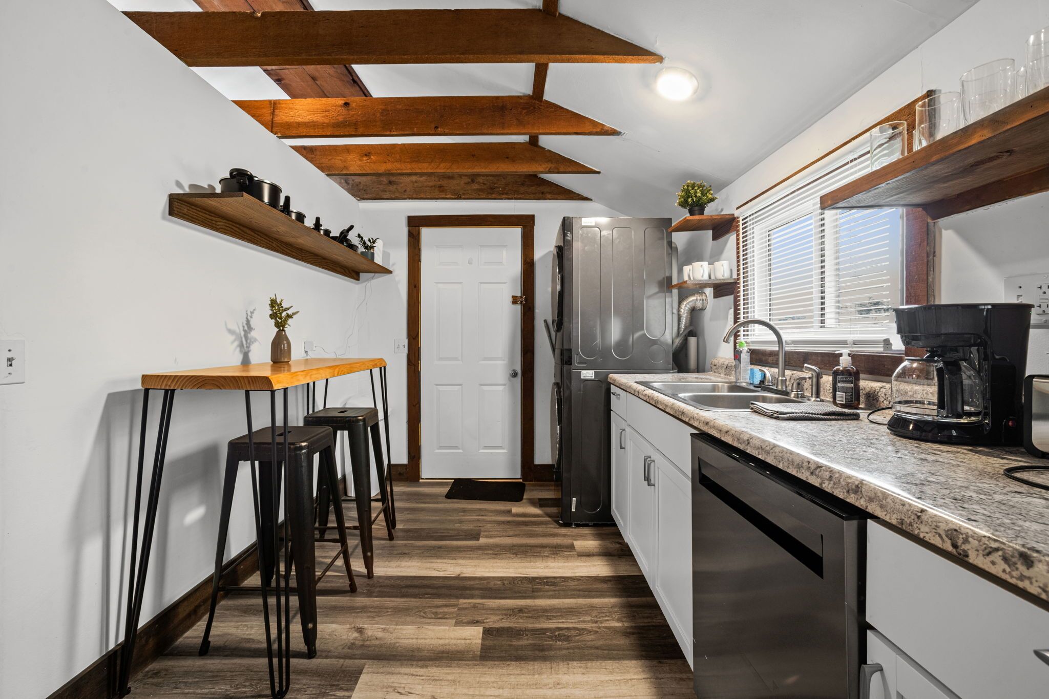 Una cocina con vigas de madera, un refrigerador, una cafetera y un ventanal con persianas.