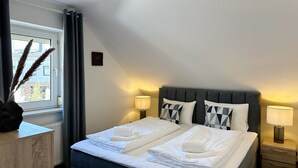 A hotel room with a bed, bedside lamps, a clock, and a window with curtains.