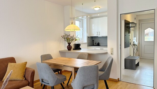 A modern living room with a wooden dining table, grey chairs, a brown leather sofa, and a glass coffee table.
