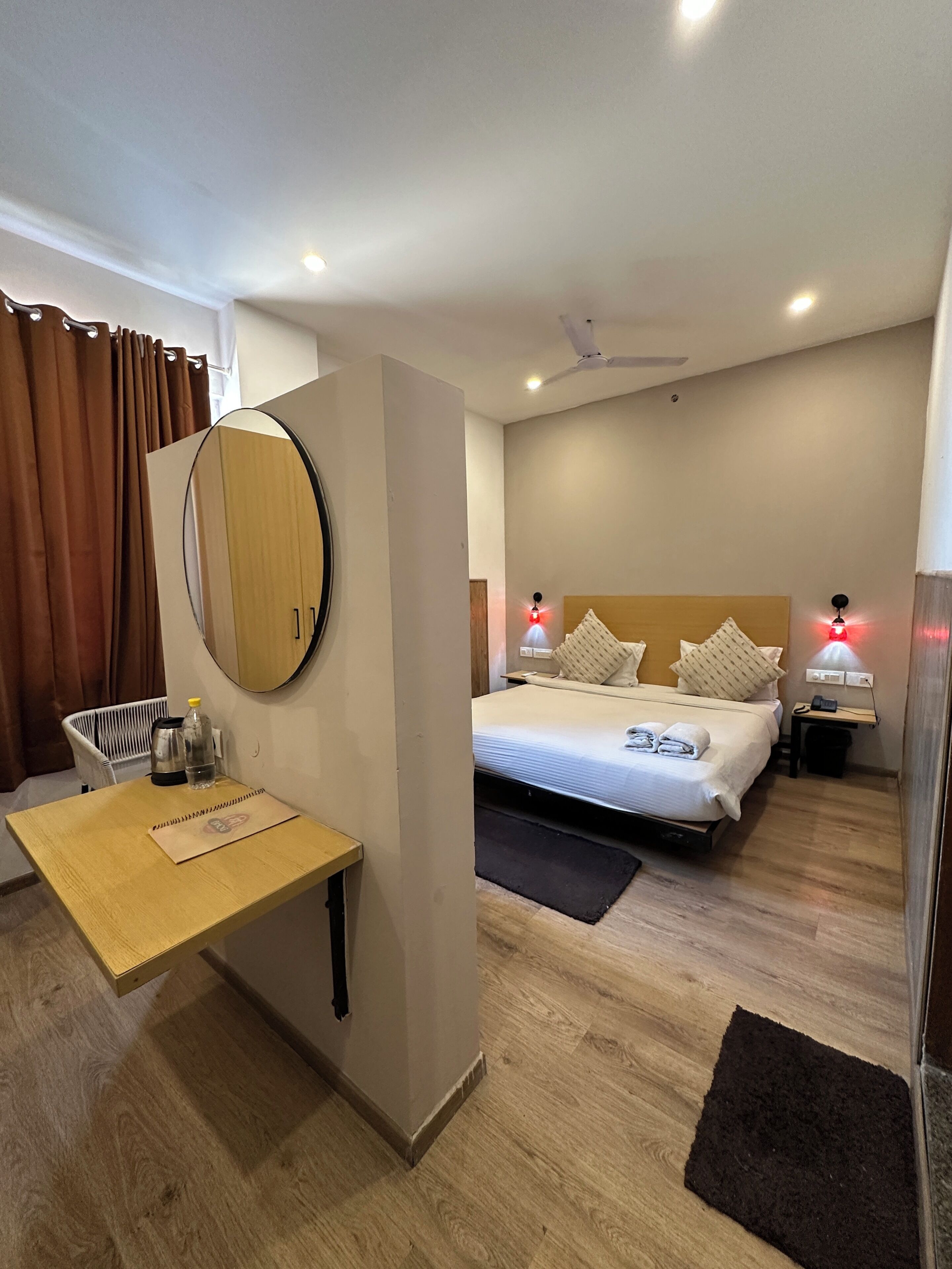 A hotel room with a bed, bedside tables, a mirror, a desk, and a chair.