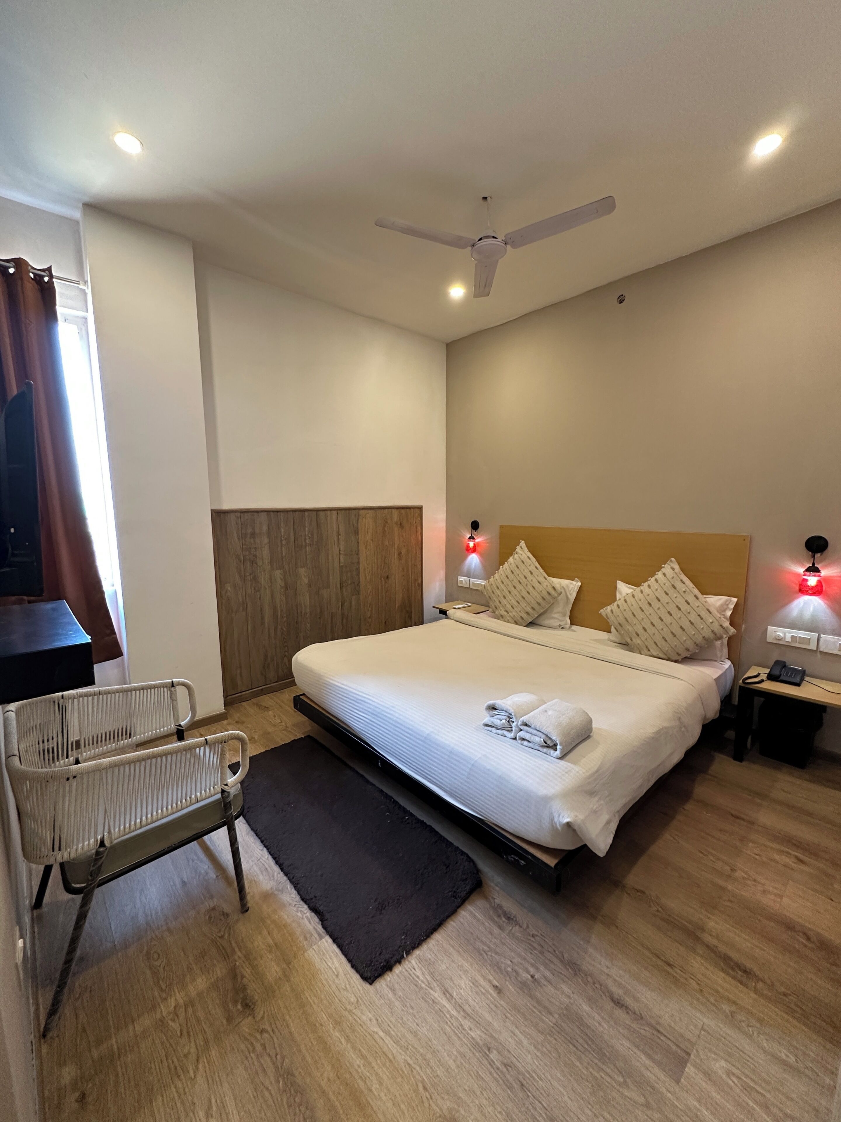 Ein Hotelzimmer mit Bett, Nachttisch, Lampe, Deckenventilator und einem Sessel.