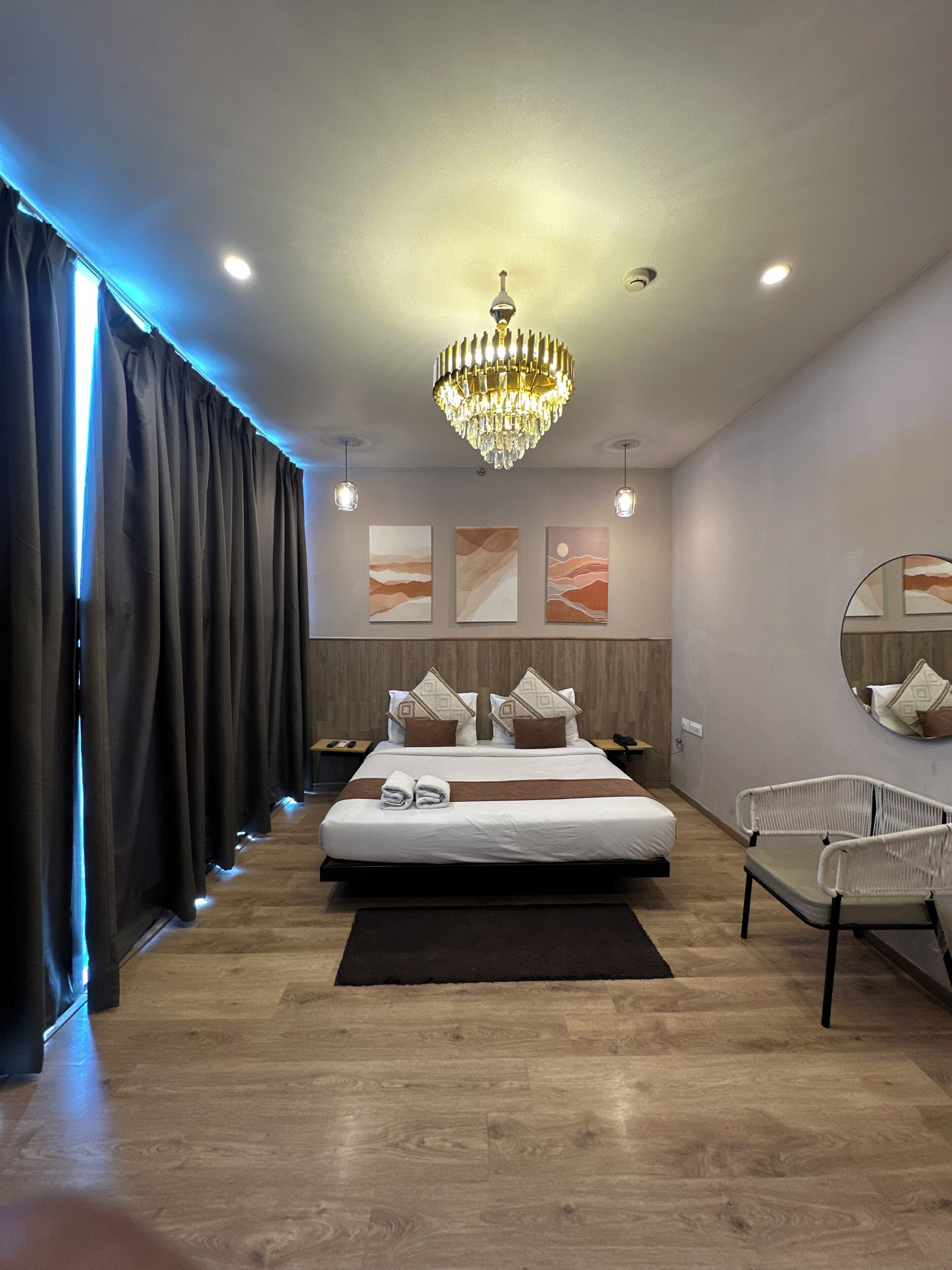 Une chambre d’hôtel moderne avec un grand lit, un lustre, des œuvres d’art au mur et un miroir rond.