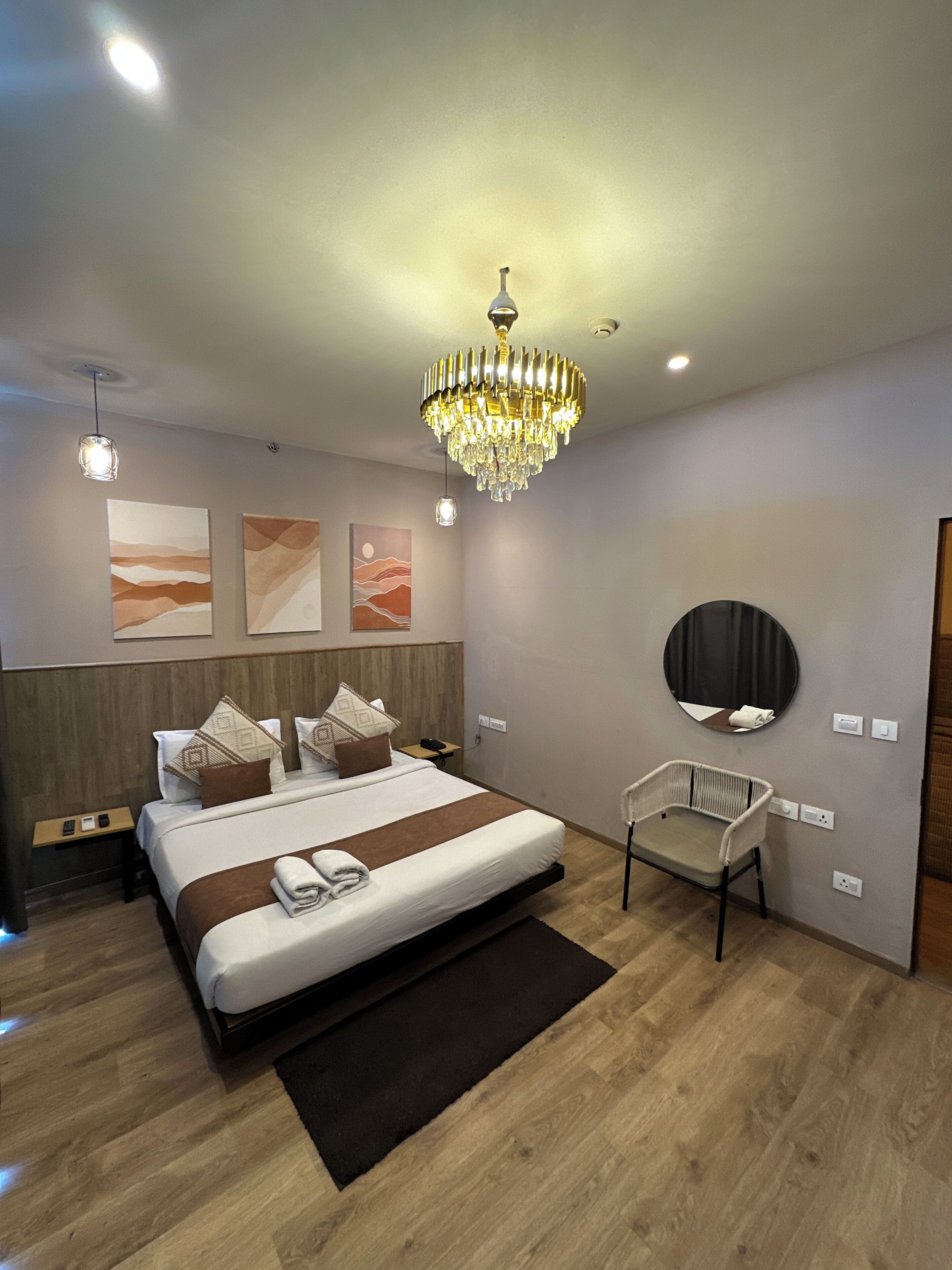 Et moderne hotelværelse med en stor seng, en lysekrone, billedkunst på væggene, et rundt spejl og et lille siddeområde.