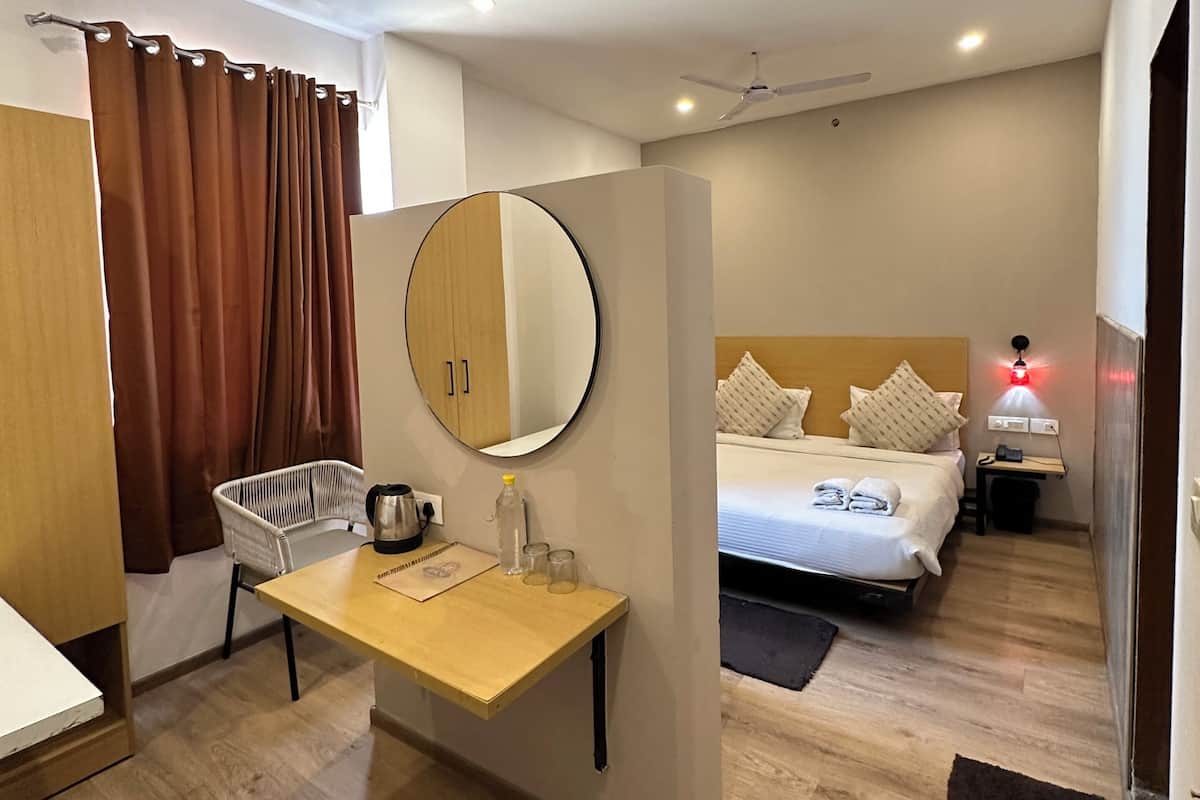 A hotel room with a wooden desk, a bed with pillows, a ceiling fan, and a nightstand with a lamp.