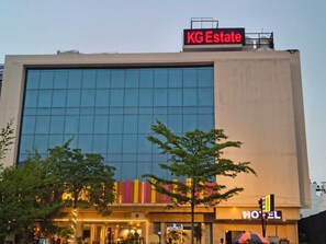 Een hotel met een grote glazen gevel, een zichtbaar bord met KG Estate erop, en een neonreclame voor het hotel.