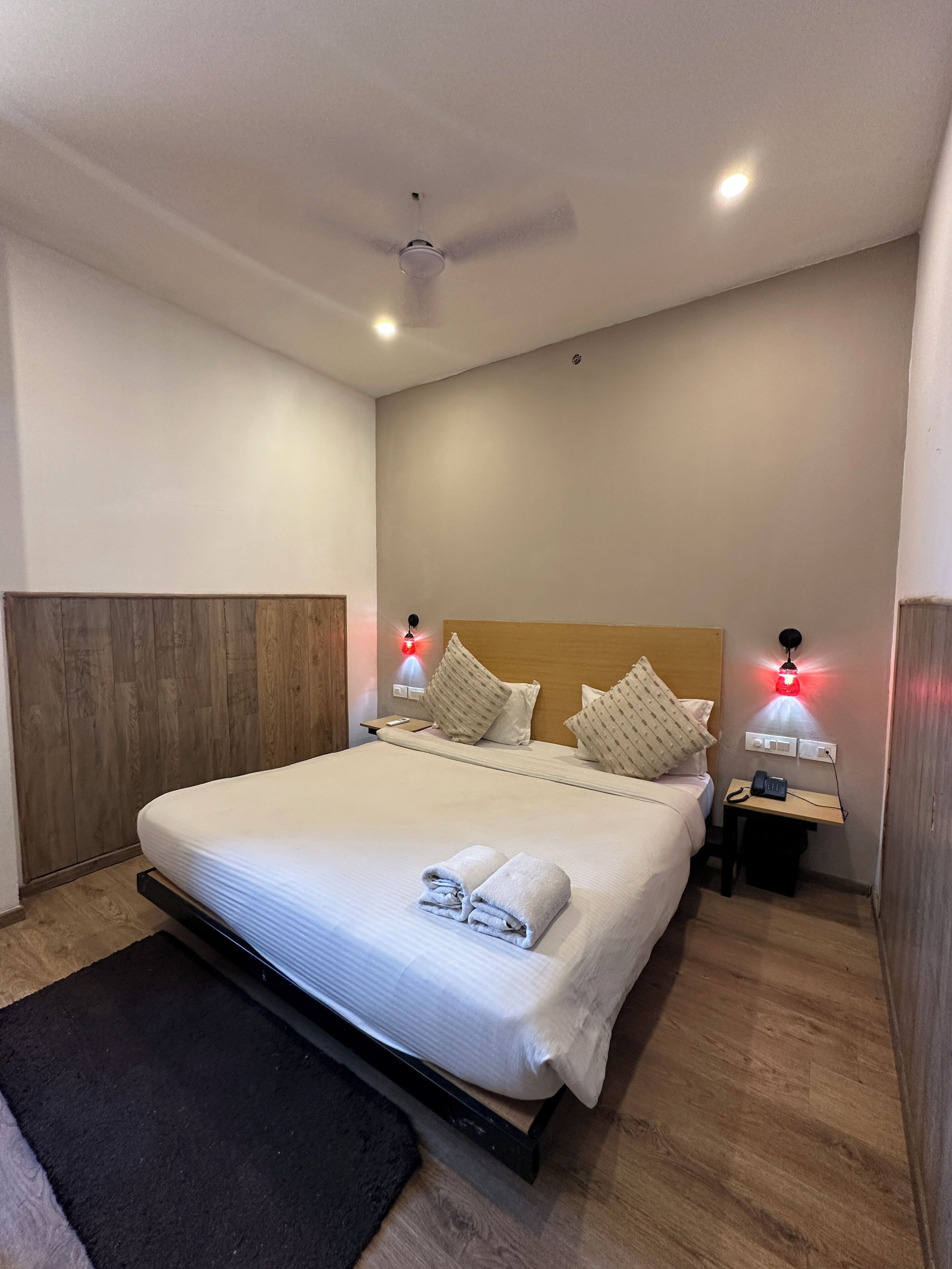 A neatly made bed with pillows, a bedside table with a phone, and a ceiling fan.