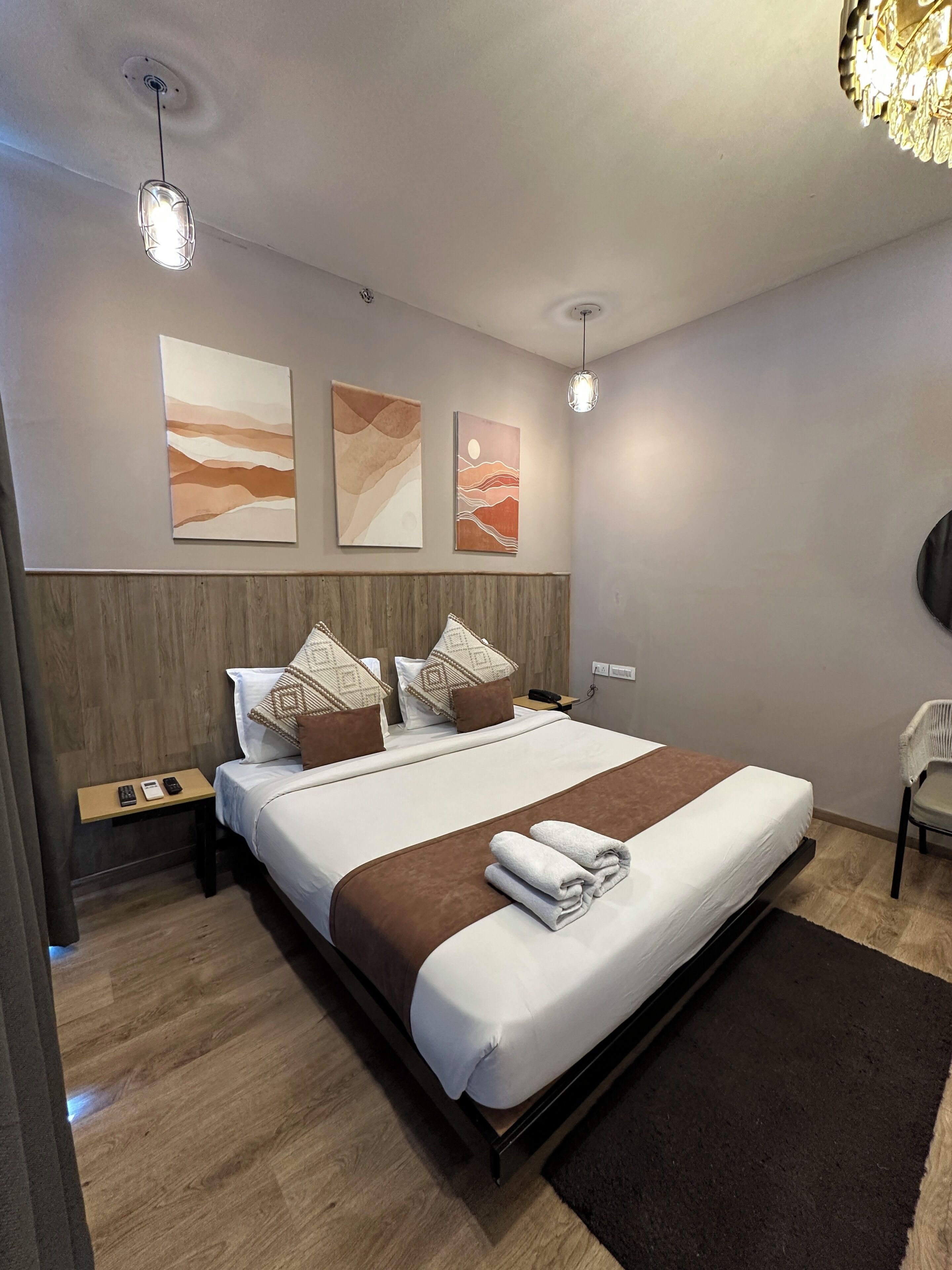 A modern hotel room with a large bed, wooden headboard, bedside tables, and artwork on the walls.