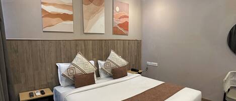 A modern hotel room with a large bed, wooden headboard, bedside tables, and artwork on the walls.