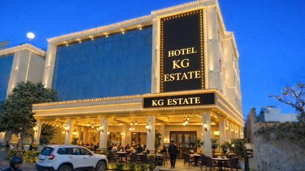 Un hotel con un cartel llamativo que dice 'KG ESTATE', asientos al aire libre y una fachada bien iluminada.