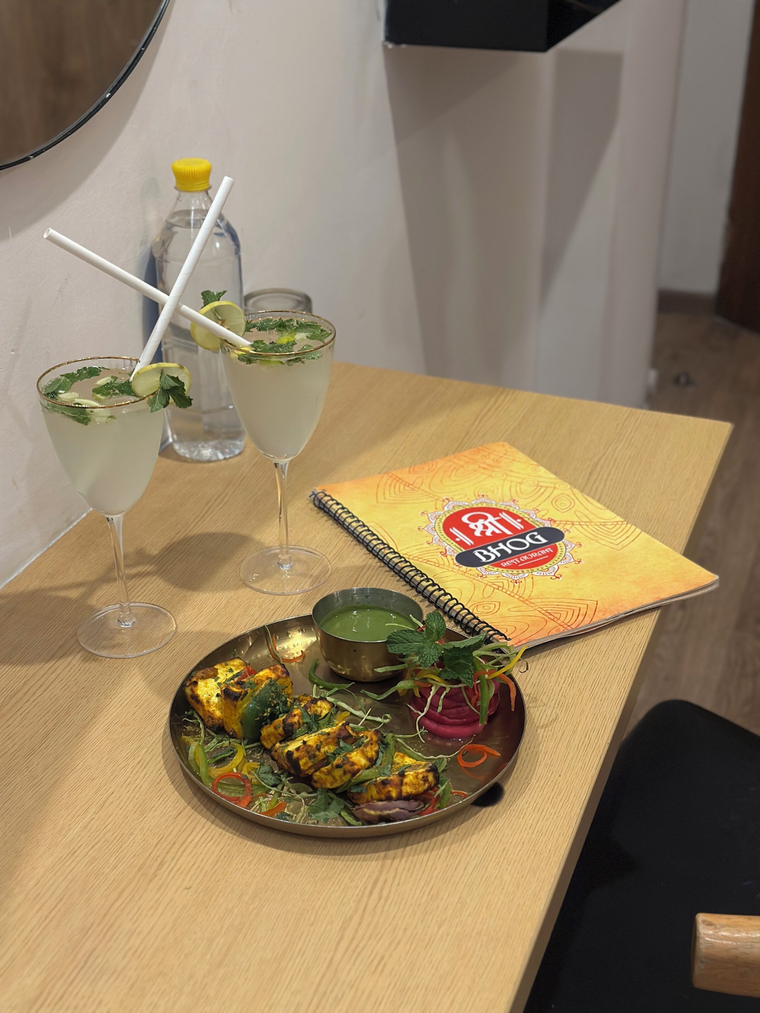 A table with a plate of food, two drinks, a bottle, and a book.